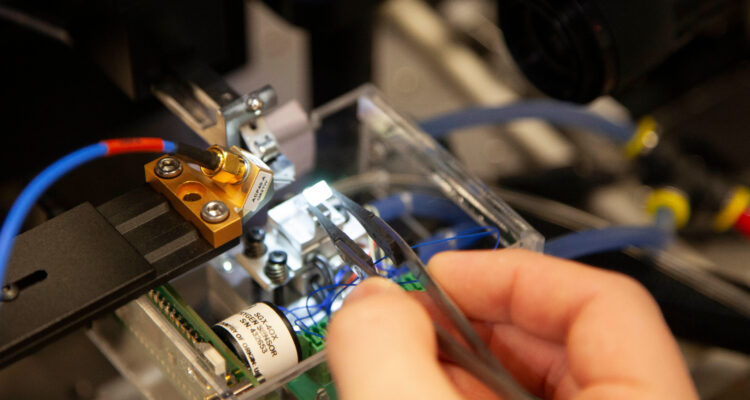 Image shows a close up of a chip being put on a probe station, Scott is holding tweezers which have the chip between them